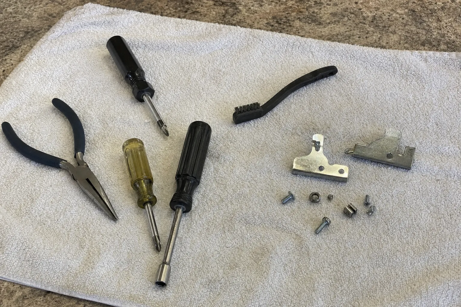 Screwdrivers, pliers, a wire brush and two stripped-out door latch plates arranged on a towel