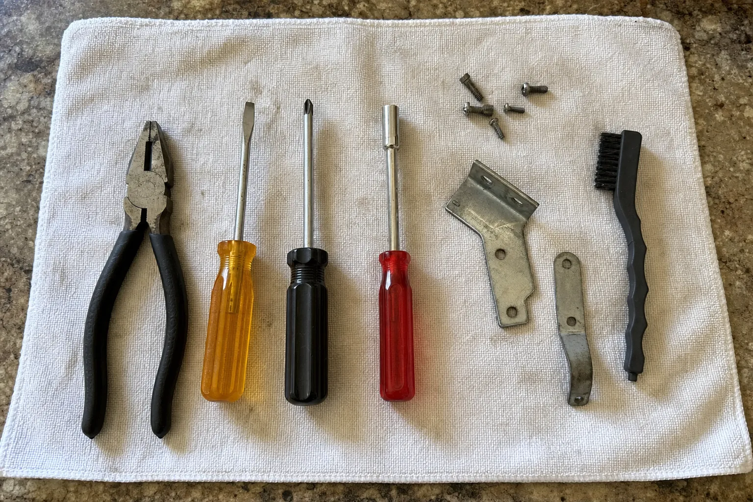 Pliers, screwdrivers, a wire brush and removed screws laid out on a towel next to a mounting bracket